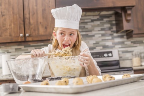 Caucasian girl tasting cookie dough in kitchen