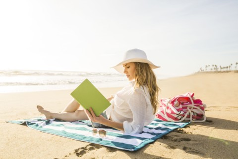 Caucasian woman reading book on beach