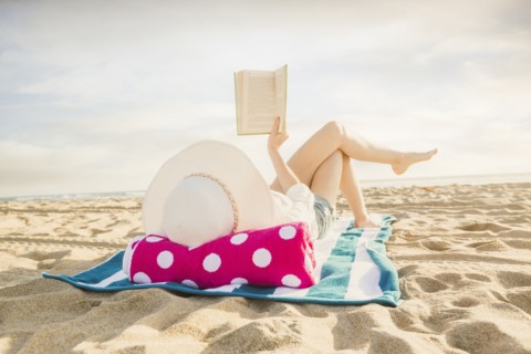 Caucasian woman reading book on beach