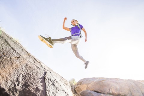 Caucasian woman leaping over boulders