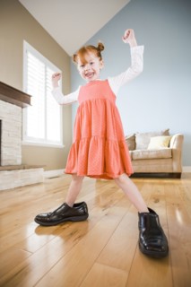 Caucasian girl wearing shoes of father in living room