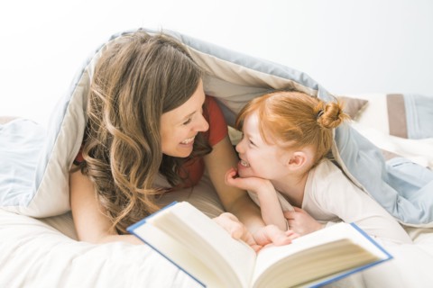 Caucasian mother and daughter reading book in bed
