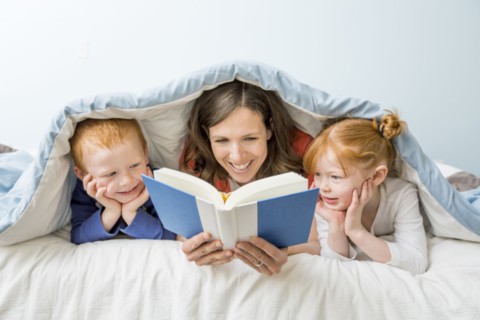 Caucasian mother and children reading book in bed