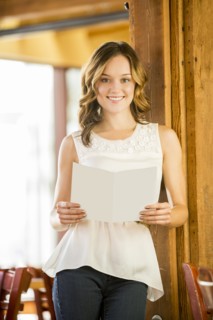 Caucasian woman leaning on beam in cafe holding menu