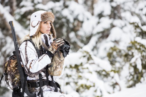 Caucasian woman hunting in forest with binoculars