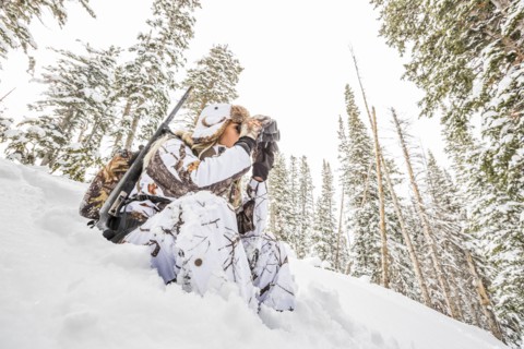 Caucasian woman hunting in forest using binoculars
