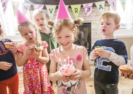 Caucasian girl wearing party hat holding cupcake with burning candles