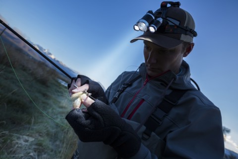 Caucasian man wearing headlamp baiting hook at dawn