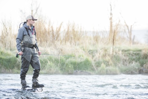 Caucasian man fly fishing on rock in river