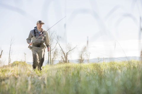 Caucasian man carrying fishing rod in field