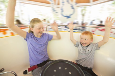 Caucasian brother and sister with arms raised on amusement park ride