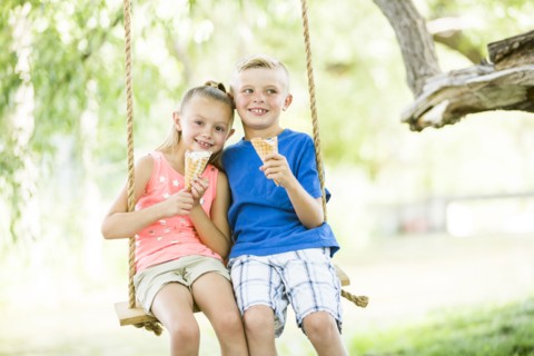 Caucasian brother and sister eating ice cream cones on rope swings