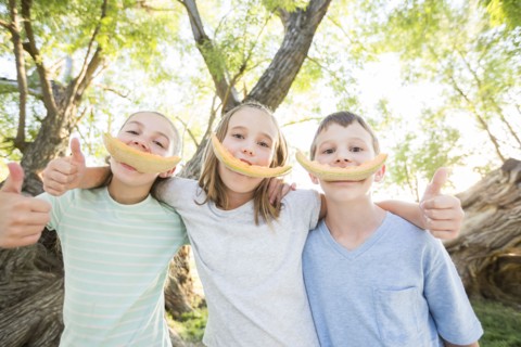 Caucasian boy and girls smiling with cantaloupe rinds