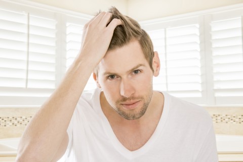 Serious Caucasian man styling hair in bathroom