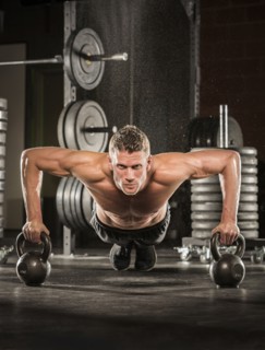Caucasian man doing push-up using kettlebells in gymnasium