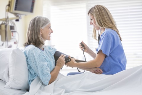 Caucasian nurse measuring blood pressure of woman in hospital bed