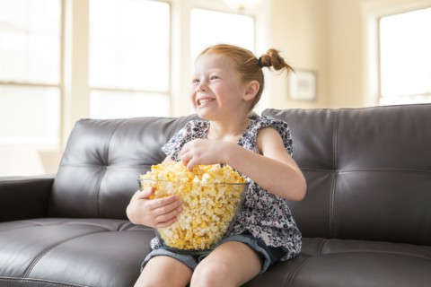 Caucasian girl sitting on sofa eating bowl of popcorn