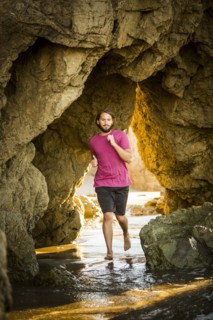 Caucasian man running under rock formation at beach