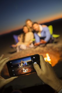 Hands of woman photographing friends on beach with cell phone