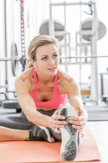 Woman stretching leg on exercise mat in gymnasium