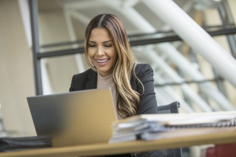 Smiling Mixed Race businesswoman using laptop