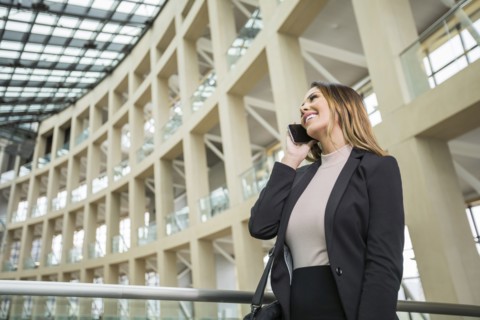 Smiling Mixed Race businesswoman talking on cell phone in lobby