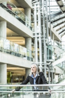 Portrait of pensive Caucasian businesswoman leaning on railing in lobby