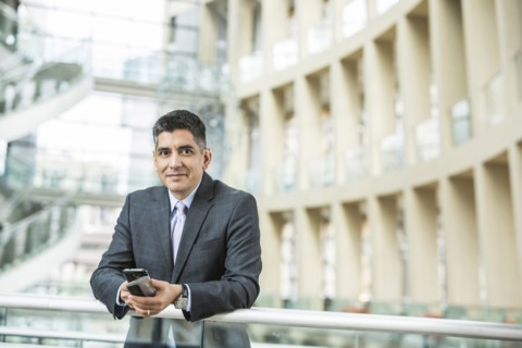 Mixed Race businessman leaning on railing in lobby holding cell phone