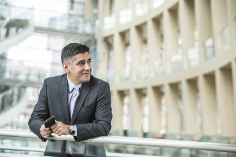 Mixed Race businessman leaning on railing in lobby holding cell phone