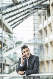 Mixed Race businessman leaning on railing in lobby talking on cell phone
