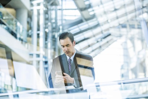 Mixed Race businessman texting on cell phone leaning on railing in lobby