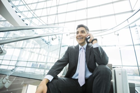 Smiling Mixed Race businessman sitting on staircase talking on cell phone