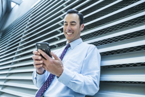 Smiling Mixed Race businessman leaning on wall texting on cell phone