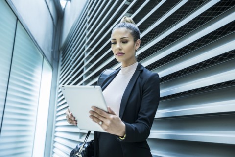 Serious Mixed Race businesswoman using digital tablet in corridor
