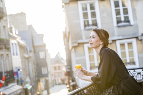 Caucasian woman drinking orange juice on balcony in city