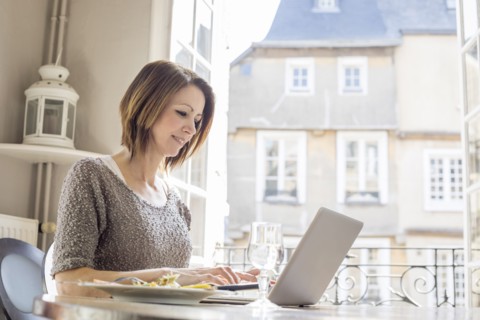 Caucasian woman typing on laptop and eating meal