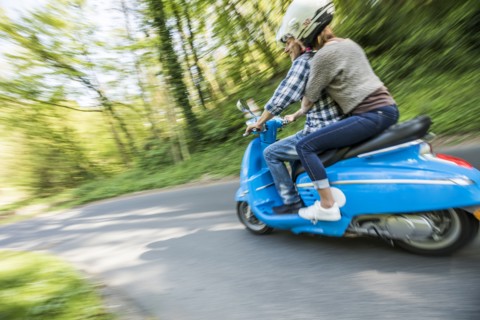Caucasian couple riding blue motor scooter