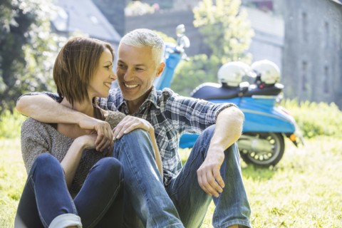 Caucasian couple sitting in grass near motor scooter