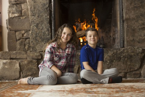 Smiling Caucasian brother and sister sitting on floor near fireplace