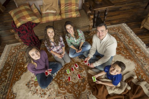 Portrait of smiling Caucasian family sitting on rug playing card game