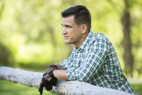 Man wearing gloves leaning on wooden fence