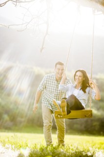 Man pushing woman swinging on tree swing