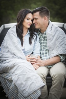 Couple wrapped in blanket sitting on bed of pick-up truck
