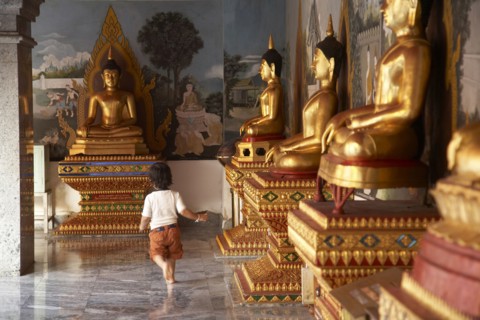 Mixed race child running past Buddha statues
