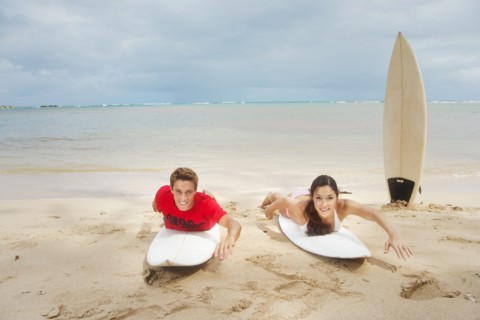 Couple laying on surfboards on beach