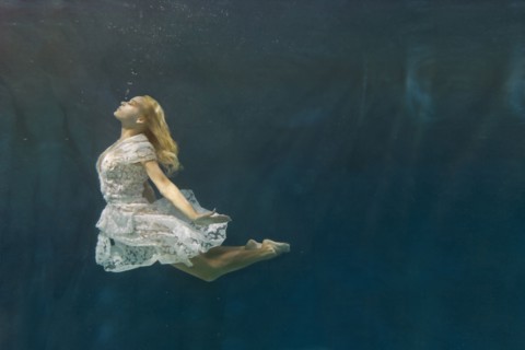 Caucasian woman in dress swimming under water