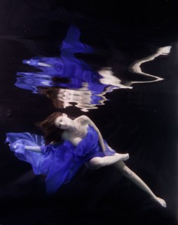 Caucasian woman in dress swimming under water