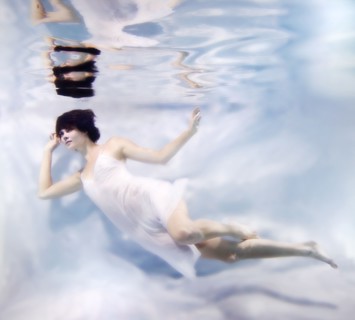 Caucasian woman in dress swimming under water