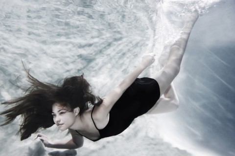 Caucasian woman in dress swimming under water