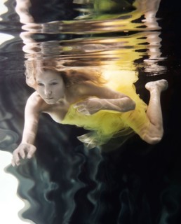 Caucasian woman in dress swimming under water